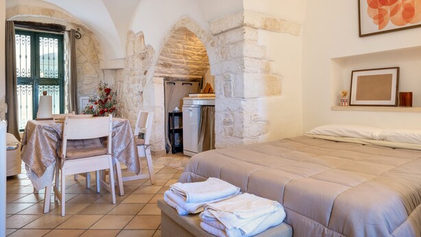 Une chambre avec un lit, une table à manger, des chaises, un coin cuisine et des murs en pierre.