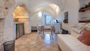 Une pièce chaleureuse avec une arche en pierre, un coin repas avec une table et des chaises, un lit avec un oreiller et un coin cuisine équipé d’un évier et de placards.