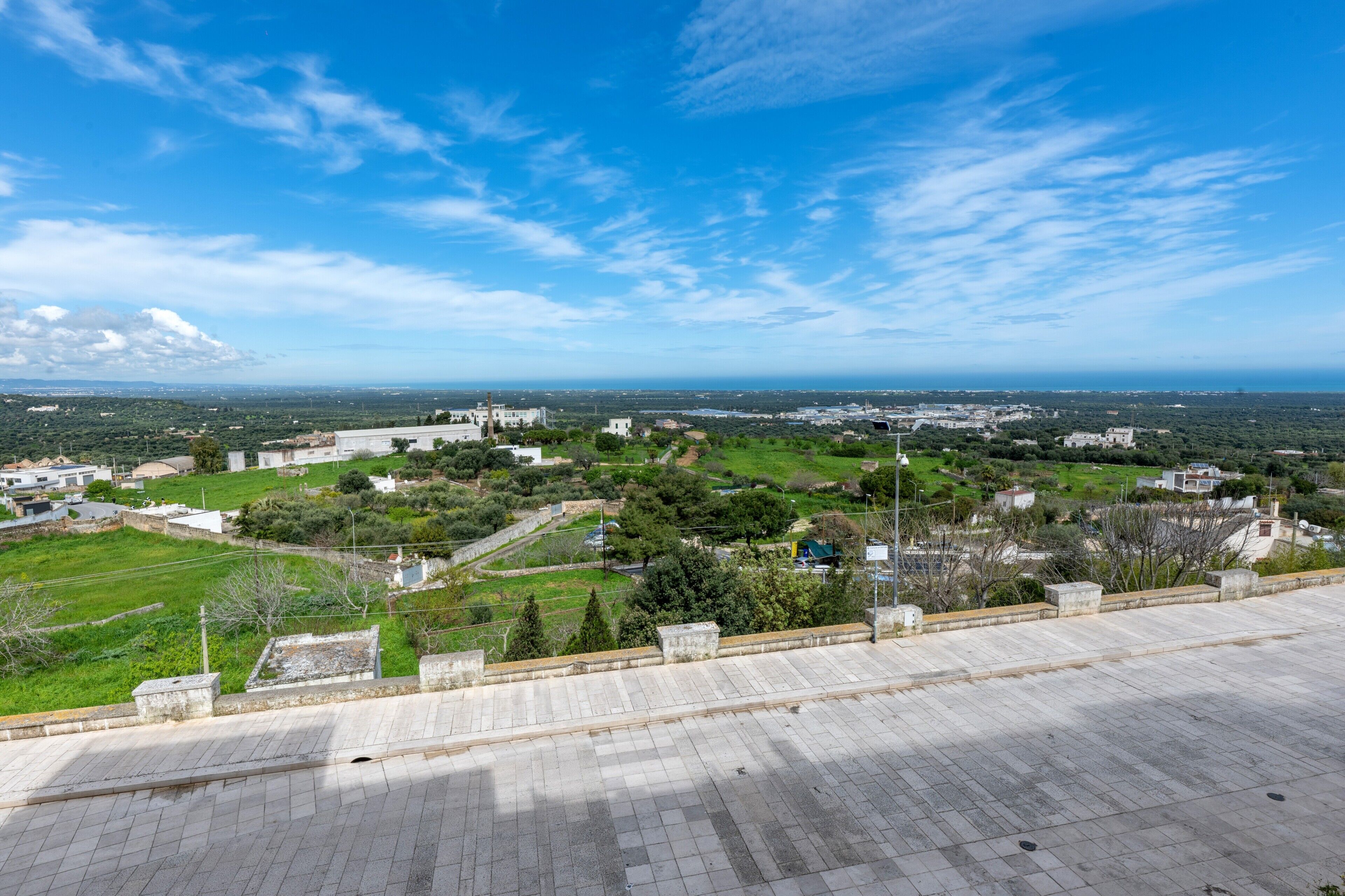 A panoramic view of a coastal town with a clear sky, featuring a mix of residential and commercial buildings, a prominent white church, and a paved walkway.