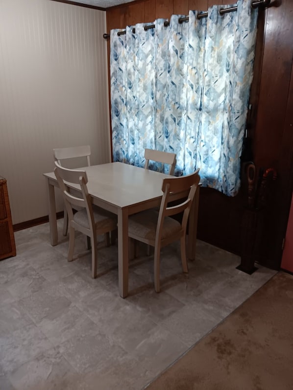 A dining area with a table and four chairs, a curtain with a geometric pattern, and a wooden door.