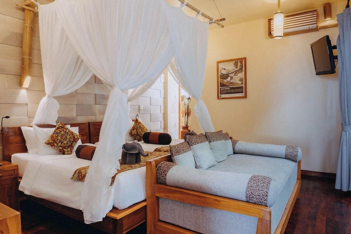 A room with two beds, one with a canopy and one without, a wooden headboard, a bedside table, and a wall-mounted TV.