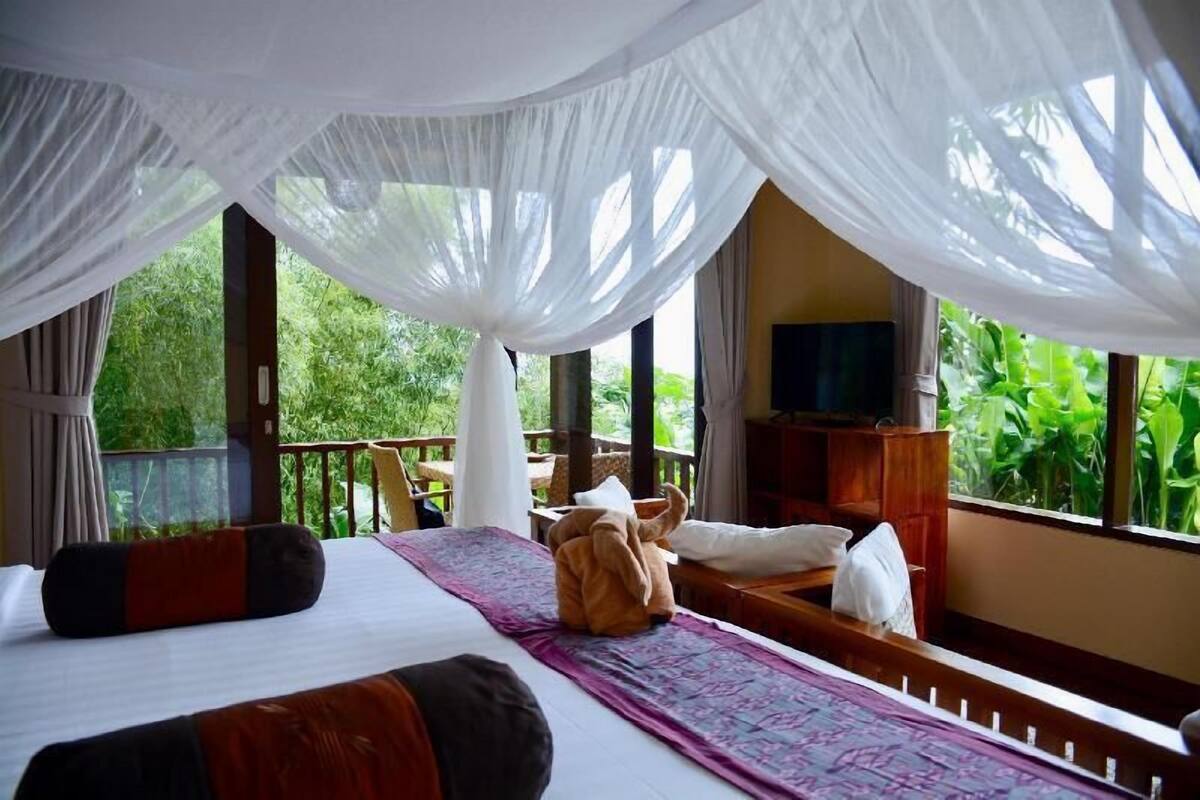 Une chambre avec un lit, une télévision, un banc en bois et une vue sur la verdure.