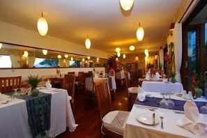 A restaurant with multiple tables, chairs, and hanging light fixtures. - Munduk Moding Plantation (Gobleg)