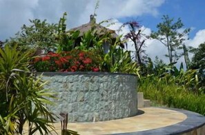 A stone structure with a curved pathway, surrounded by lush greenery and a gazebo.