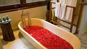A bathtub filled with red rose petals, a wooden stool, and a towel rack. - Munduk Moding Plantation (Gobleg)