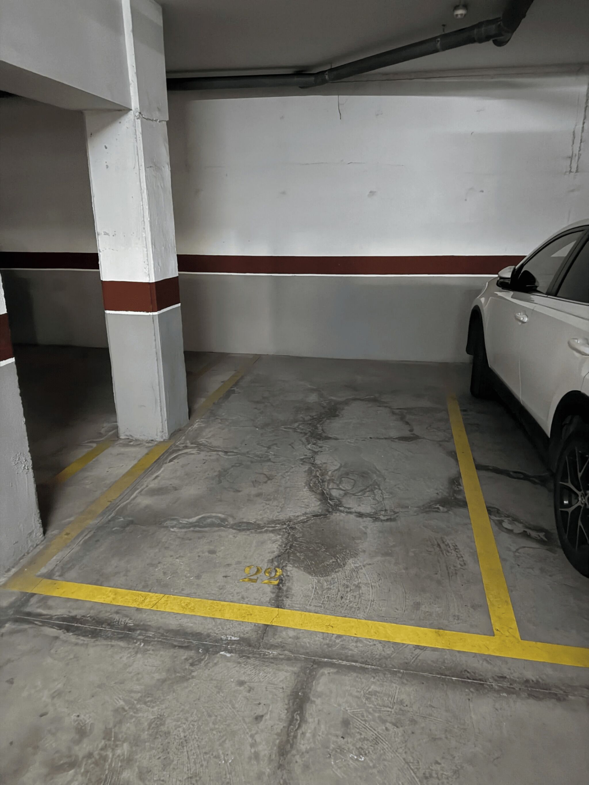 Een parkeergarage met betonnen vloeren, witte pilaren en een witte auto geparkeerd op een parkeerplaats.