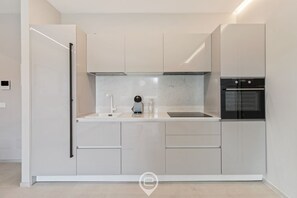 A modern kitchen with white cabinetry, a built-in oven, and a coffee maker. - Appartamento Ginevra 3 (Arzachena)