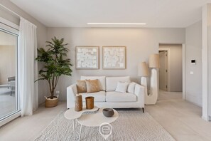 A modern living room with a white sofa, a coffee table, a potted plant, and abstract wall art. - Appartamento Ginevra 3 (Arzachena)