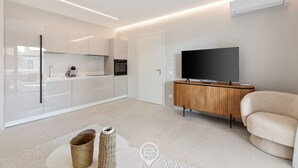 Une cuisine moderne avec des meubles blancs, un four encastré et un téléviseur à écran plat posé sur un meuble en bois.