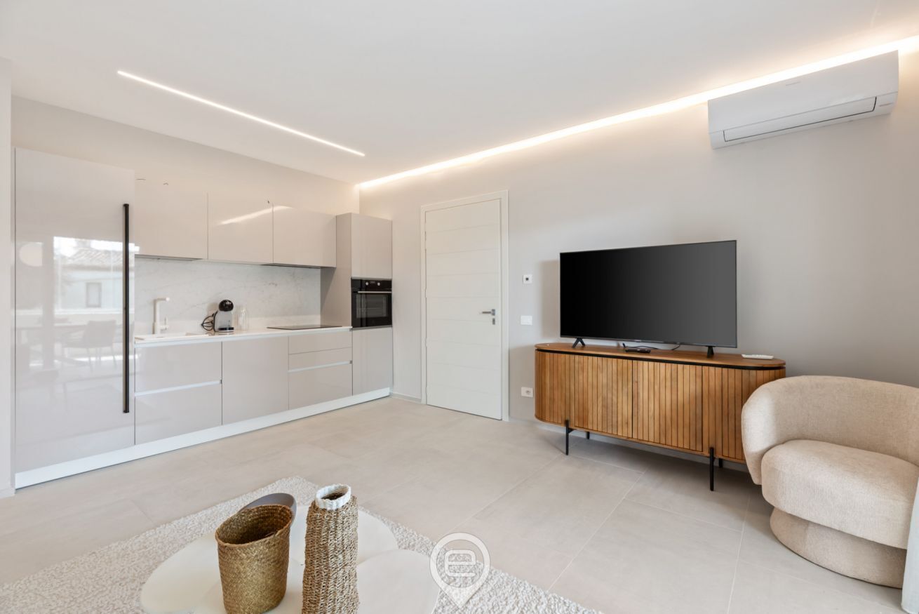 A modern kitchen with white cabinets, a built-in oven, and a flat-screen TV on a wooden cabinet. - Appartamento Ginevra 3 (Arzachena)