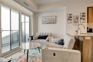 A modern living room with a sofa, a coffee table, and a view through large glass doors. - Modern High-rise Condo w City Views Balcony (Kitchener)