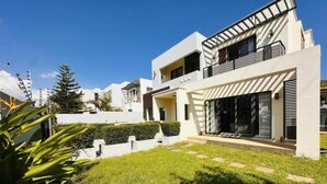Ein modernes, zweistöckiges Haus mit gepflegtem Rasen, einer überdachten Terrasse und einem großen Schiebetürfenster.