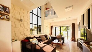 Ein geräumiges Wohnzimmer mit einem Ecksofa, einem Flachbildfernseher und einem Balkon mit Geländer.