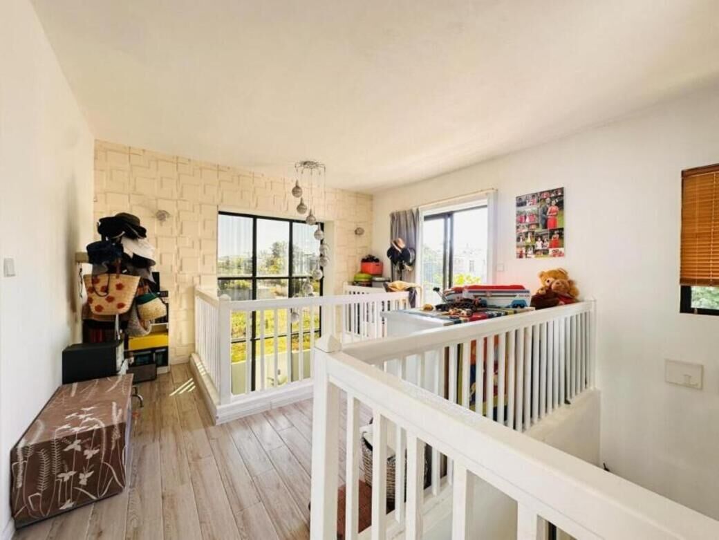 Une pièce spacieuse avec un plafond haut, une balustrade blanche, une grande fenêtre et une vue sur l’extérieur.