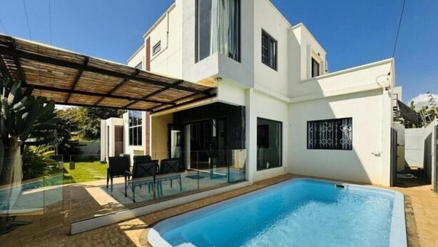 Ein modernes, zweistöckiges Haus mit Swimmingpool, Glasüren und einer überdachten Terrasse.