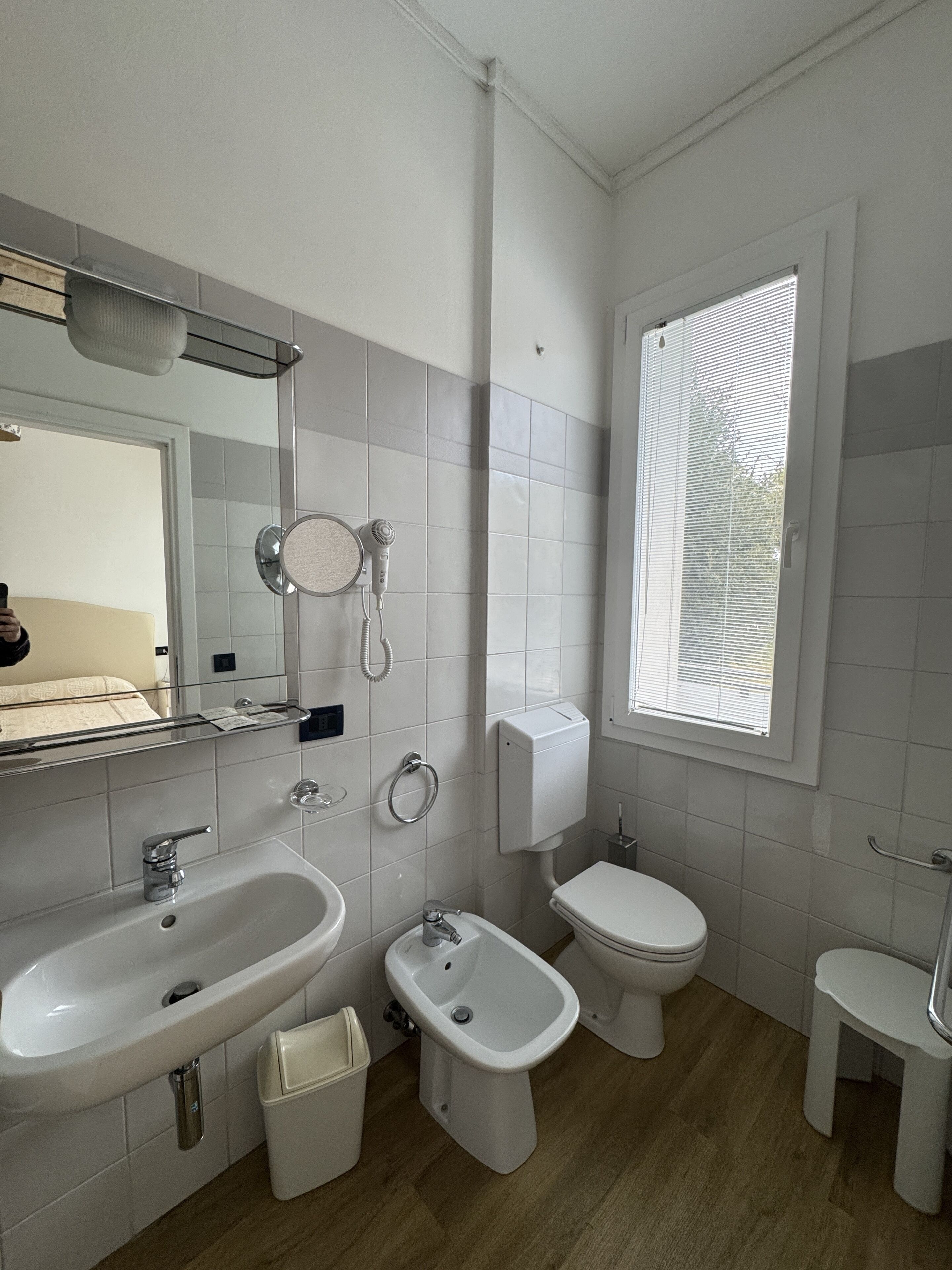 A modern bathroom with a sink, bidet, toilet, and a window providing natural light.
