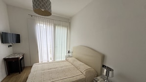 Une chambre à coucher comprenant un lit, une table de chevet, une lampe, un téléviseur fixé au mur et une fenêtre avec des rideaux.