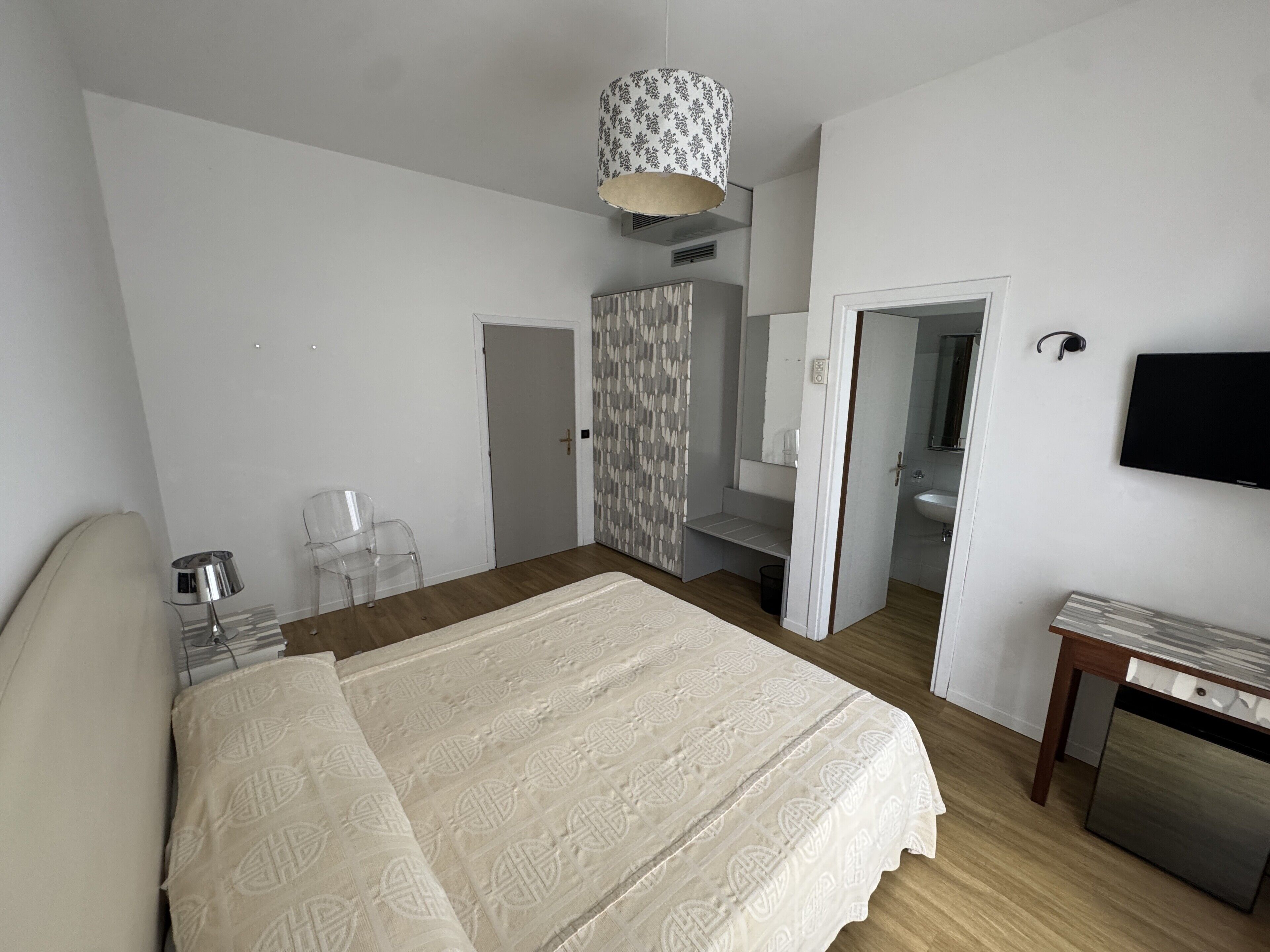 Una camera da letto con un letto, una scrivania, una sedia, una televisione e l'ingresso del bagno.