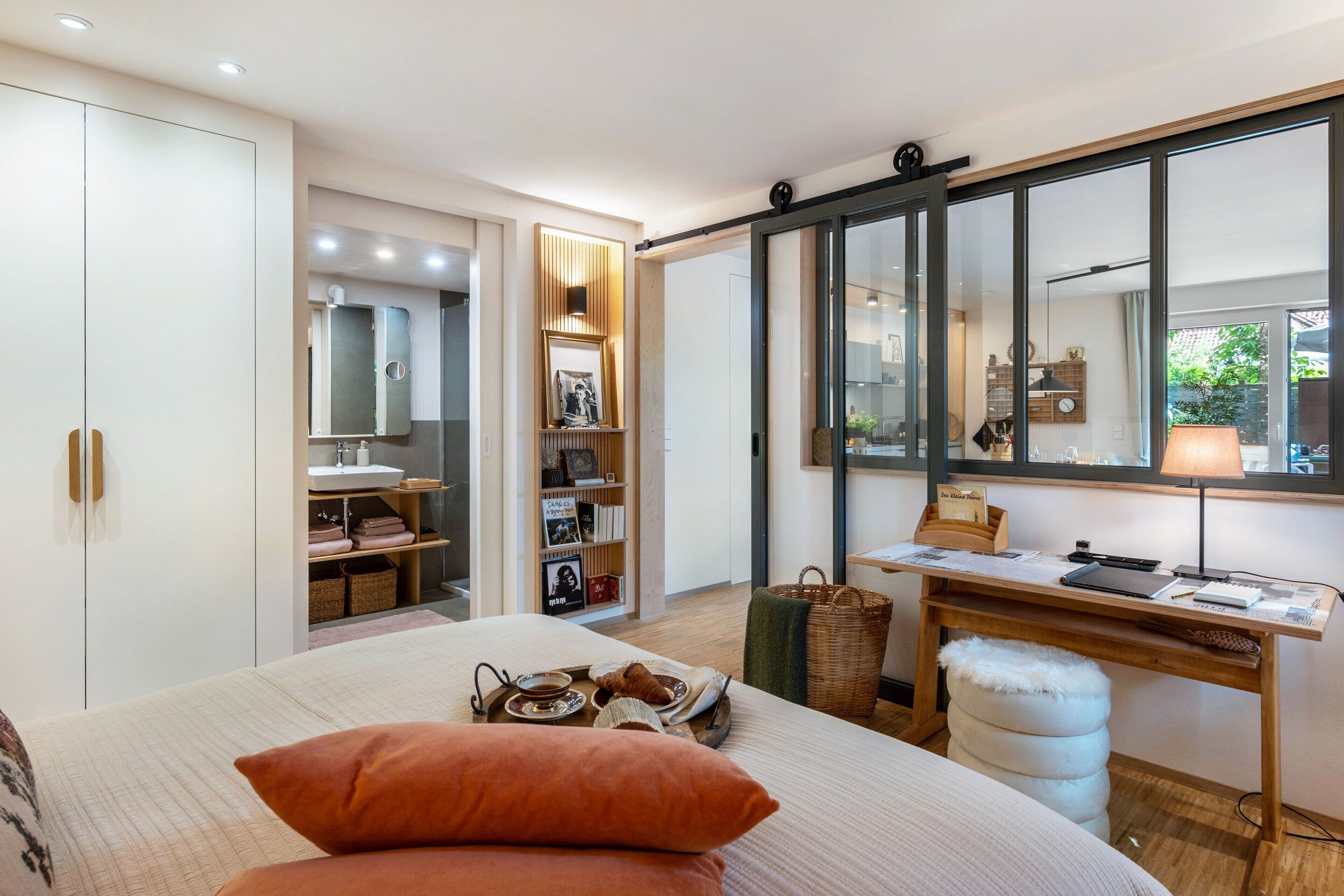 Ein Schlafzimmer mit Bett, Schreibtisch, Spiegel, Kleiderschrank und eigenem Bad.