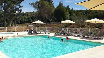 A swimming pool with lounge chairs and umbrellas, surrounded by a fence and trees.