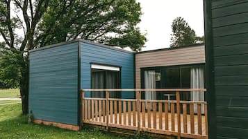 Une petite cabane avec une terrasse en bois et une grande fenêtre.