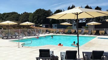 Une piscine entourée d’une clôture et d’arbres, avec des chaises longues et des parasols.
