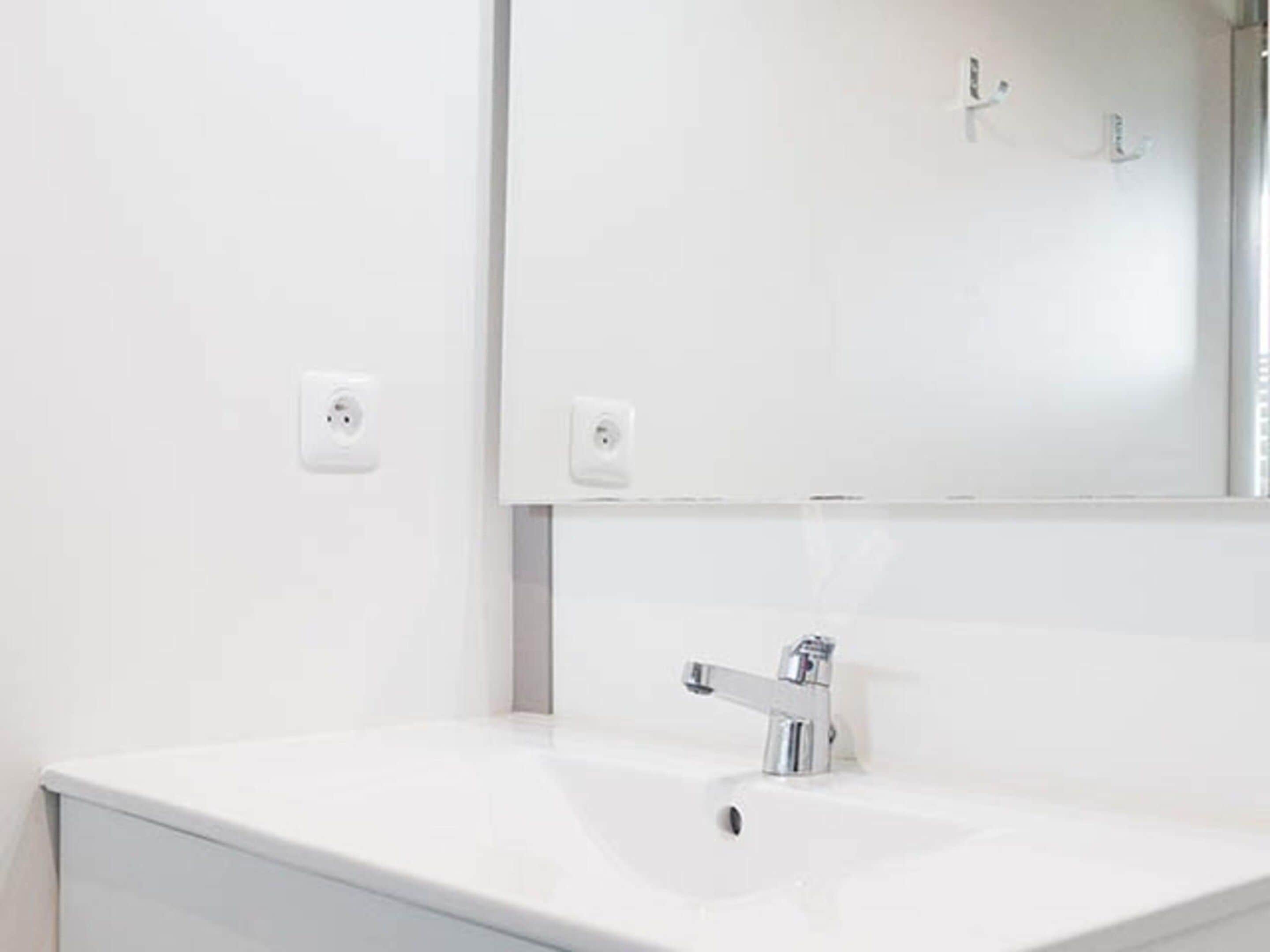 Une salle de bain avec un lavabo blanc, un miroir et un robinet.