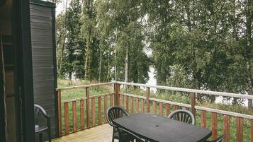 Une terrasse en bois avec une table et des chaises, donnant sur une étendue d’eau et entourée d’arbres.
