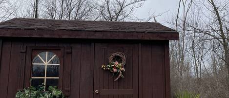 A small wooden building with a window, a door with a wreath, and a potted plant.