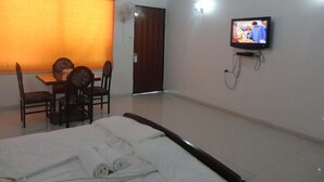 Quarto de hotel com cama, televisão, mesa de jantar com cadeiras e janela com cortinas.