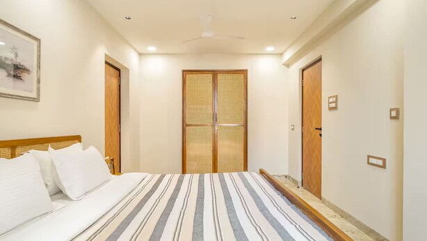 Habitación de hotel con cama, ventilador de techo y puerta con panel tejido.