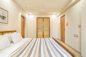 A hotel room with a bed, a ceiling fan, and a door with a woven screen. - Chic 2bhk in Candolim 5 Min to Beach Pool Gym (Candolim)