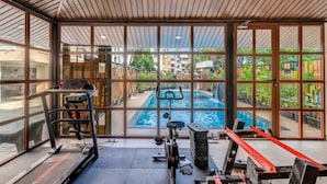 Un gimnasio con equipo de ejercicio, ventanas amplias y vistas a una piscina.