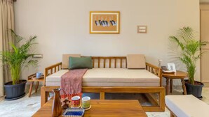 Una habitación con un sofá, una mesa de centro, dos plantas en macetas, un cuadro en la pared y una pequeña mesa con una taza y un libro.