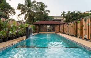 Ein Schwimmbecken mit Wasserfall, umgeben von einem Holzzaun und Palmen.