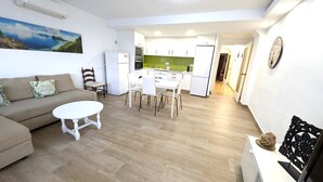 Sala de estar com sofá, mesa redonda e conjunto de jantar. Cozinha com armários brancos e painel verde.