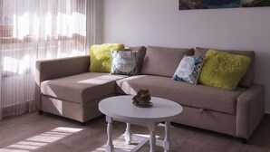 Uma sala de estar moderna com um sofá bege, uma mesa de centro branca e almofadas decorativas.