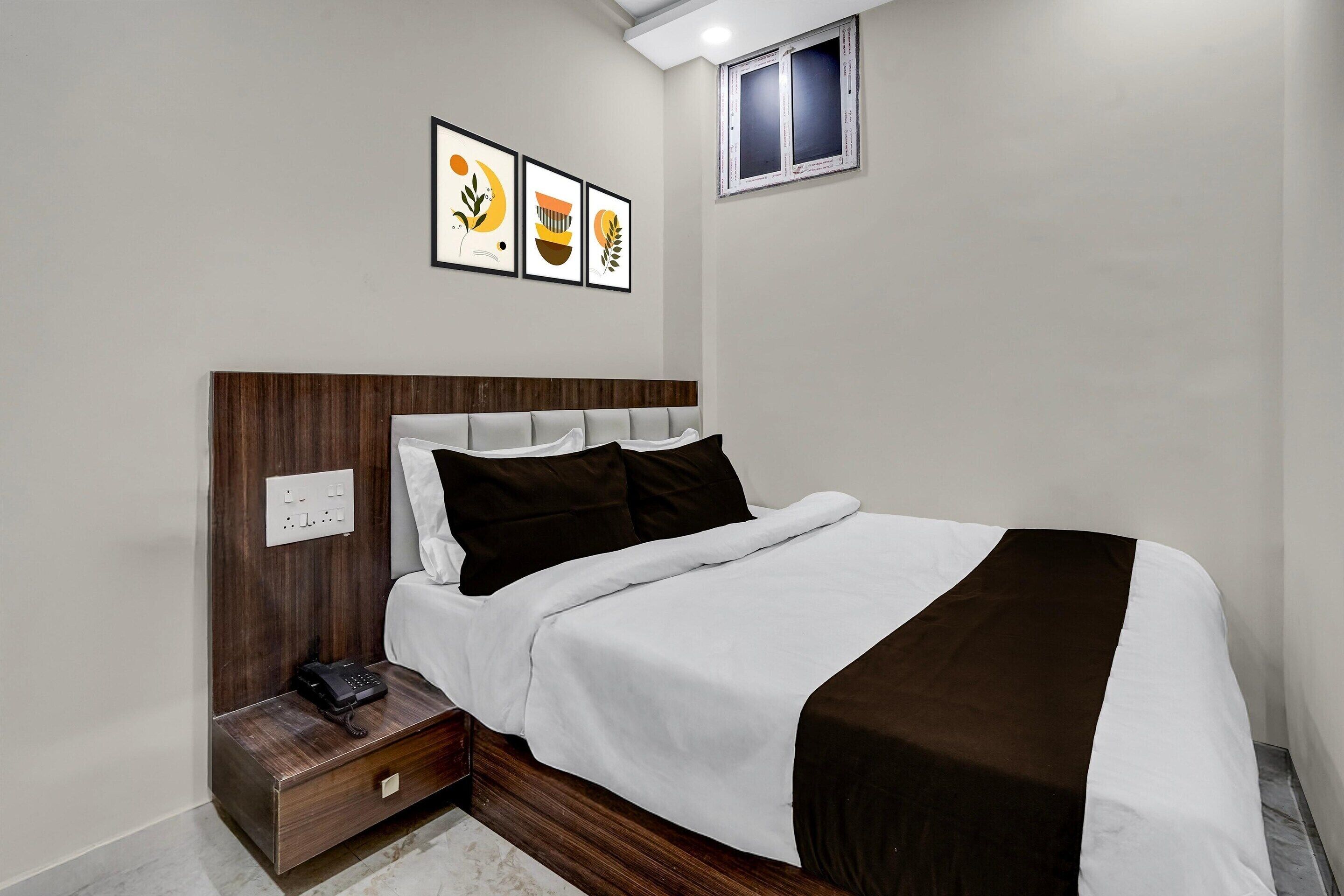 A neatly made bed with a wooden headboard, a bedside table with a phone, and a small window.