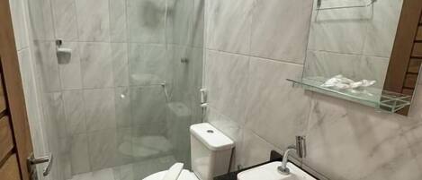Casa de banho com chuveiro envidraçado, sanita branca, lavatório preto e espelho sobre o lavatório.