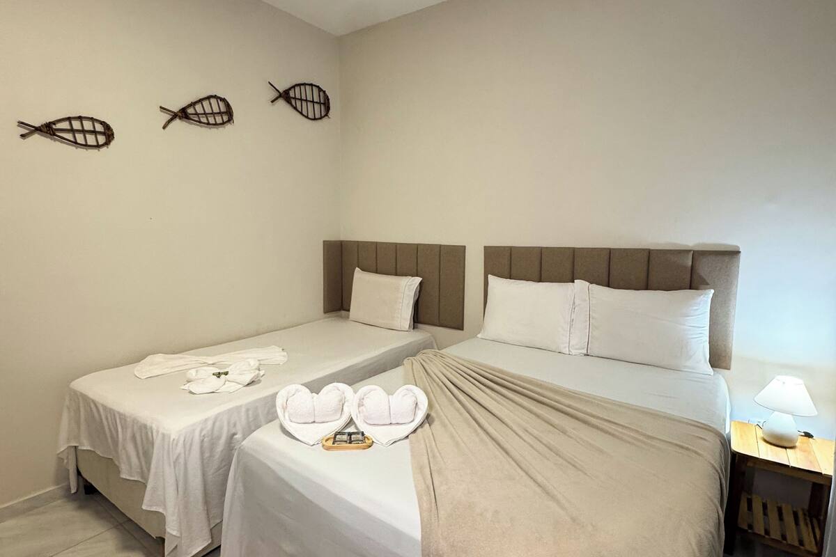 Una habitación de hotel con dos camas, una mesita de noche con lámpara y una cesta tejida en el suelo.