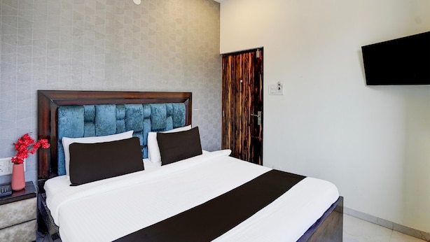 Ein Hotelzimmer mit einem großen Bett, einem Nachttisch, einer Blumenvase und einem an der Wand befestigten Fernseher.