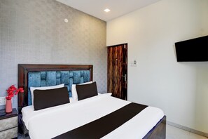 A hotel room with a large bed, a nightstand, a vase of flowers, and a television on the wall. - Super Itwari Station Formerl Hotel Prime (Nagpur)