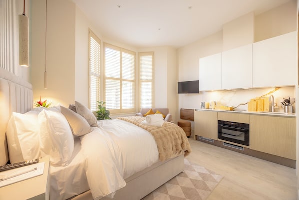 A modern bedroom with a large bed, bedside tables, a flat-screen TV, and a built-in oven.