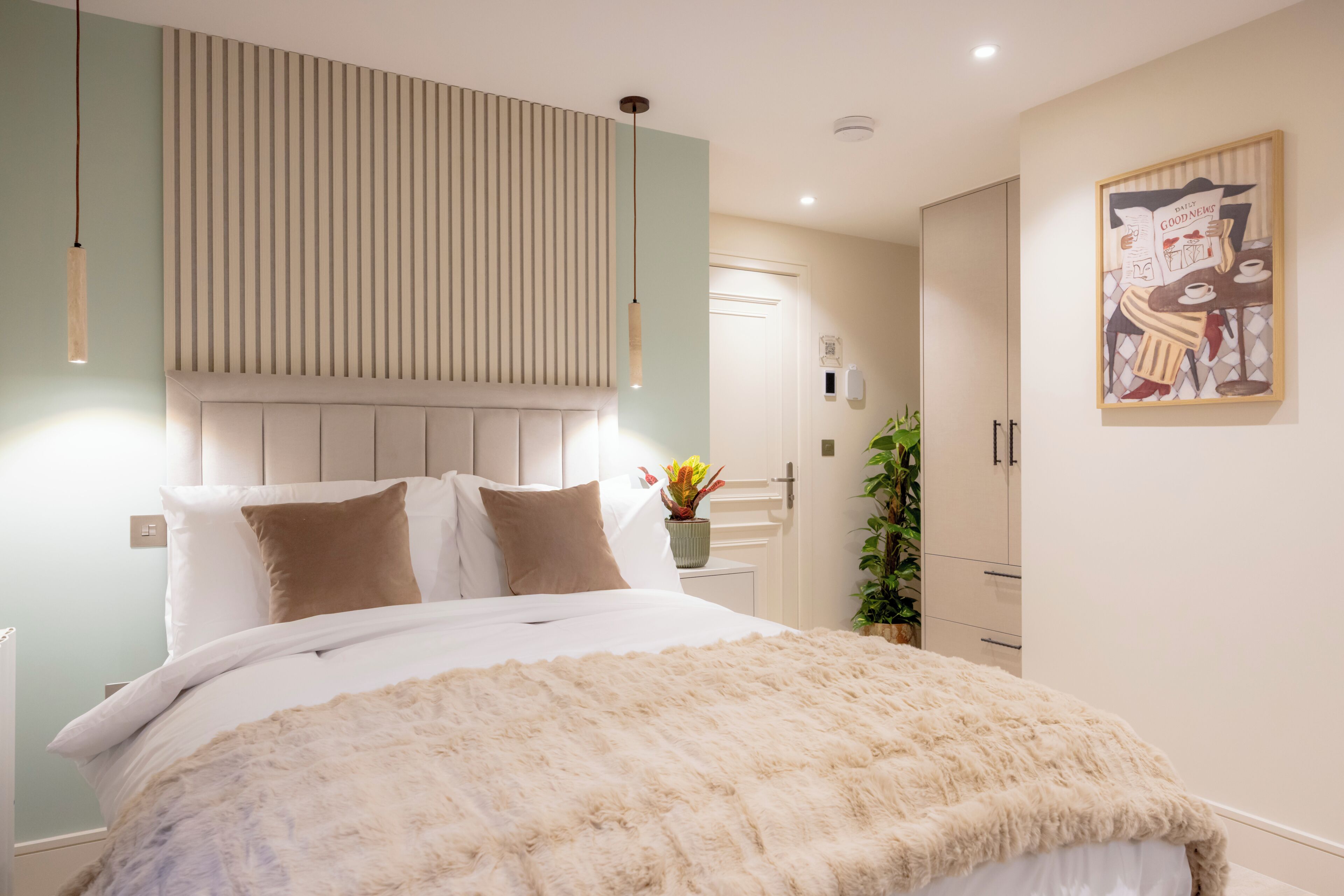 Ein modernes Schlafzimmer mit Bett, Nachttischen, einer Wandleuchte, einer Pflanze und einem gerahmten Bild.