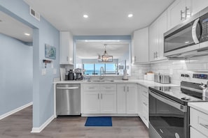 A modern kitchen with white cabinets, stainless steel appliances, and a blue accent wall. - ☀Stunning Views🐬Beachfront Condo🌴Ocean Sands II-602🐠Heated Pool/Hot Tub/Grills (Madeira Beach)
