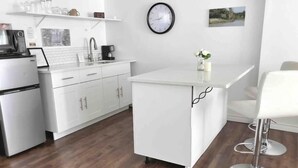 A modern kitchen with white cabinetry, a coffee machine, a microwave, and a clock on the wall.