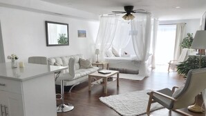 A modern bedroom with a canopy bed, a sitting area with a sofa and armchairs, a desk, and a bedside table.