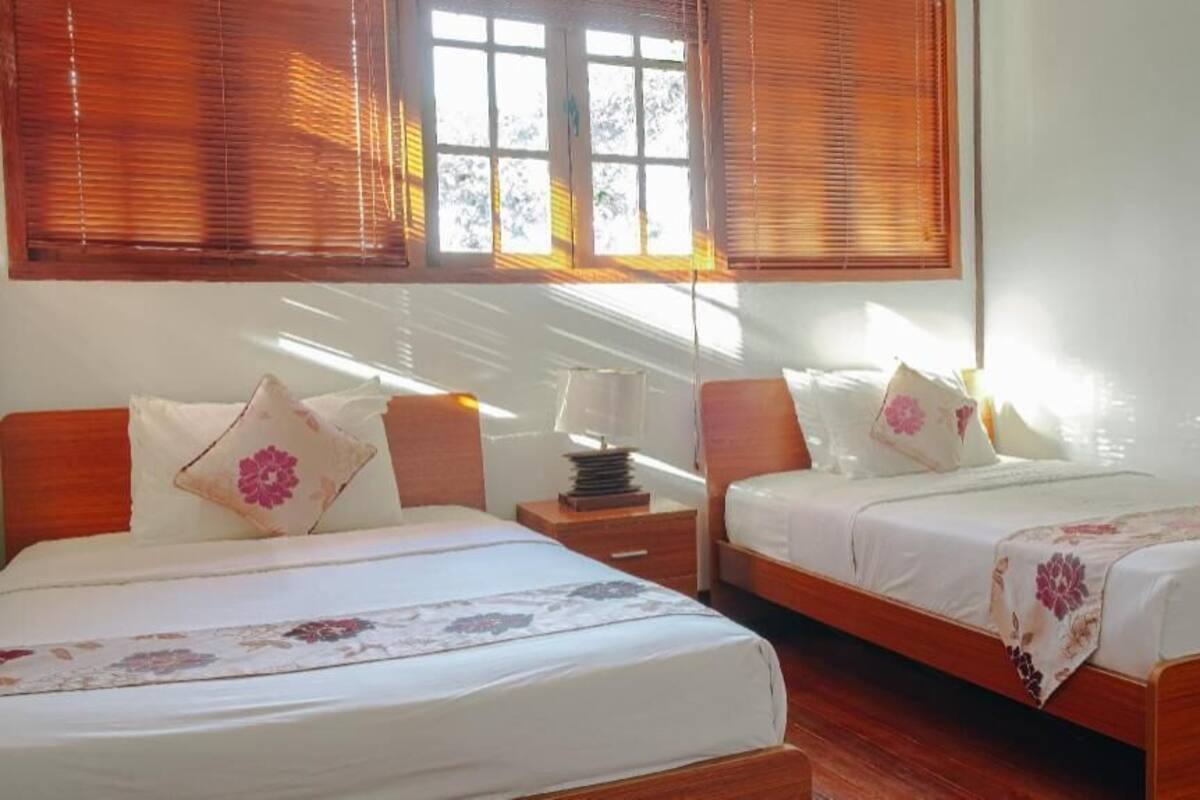 A room with two beds, wooden headboards, and a window with blinds.