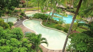 Ett semesterparadis med en stor, slingrande pool omgiven av palmer och frodig grönska.
