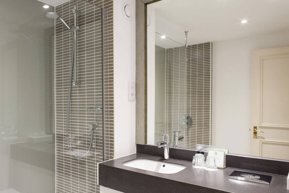 Un baño moderno con cabina de ducha de vidrio, un lavamanos con encimera oscura y un espejo grande que refleja la habitación.
